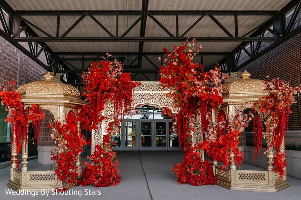 wedding entrance decor,red floral installation,indian wedding mandap entrance,luxury wedding design,ornate pillars decor,bold wedding colors,floral statement backdrop,grand entrance setup,event design details,wedding venue styling