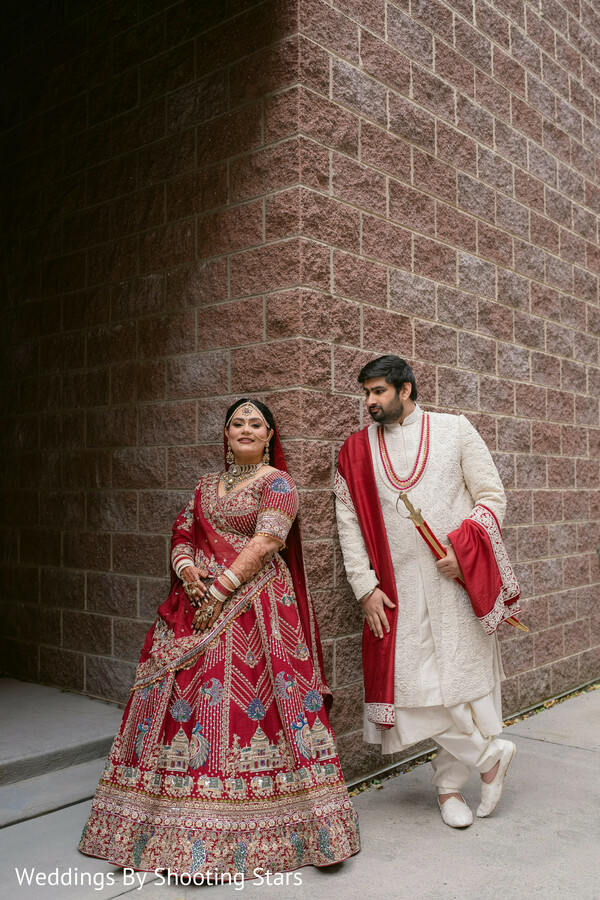 bride red lehenga,groom ivory sherwani,editorial couple portrait,urban backdrop wedding,brick wall texture,indian wedding fashion,modern couple pose,stylish wedding portrait,cultural attire,romantic candid