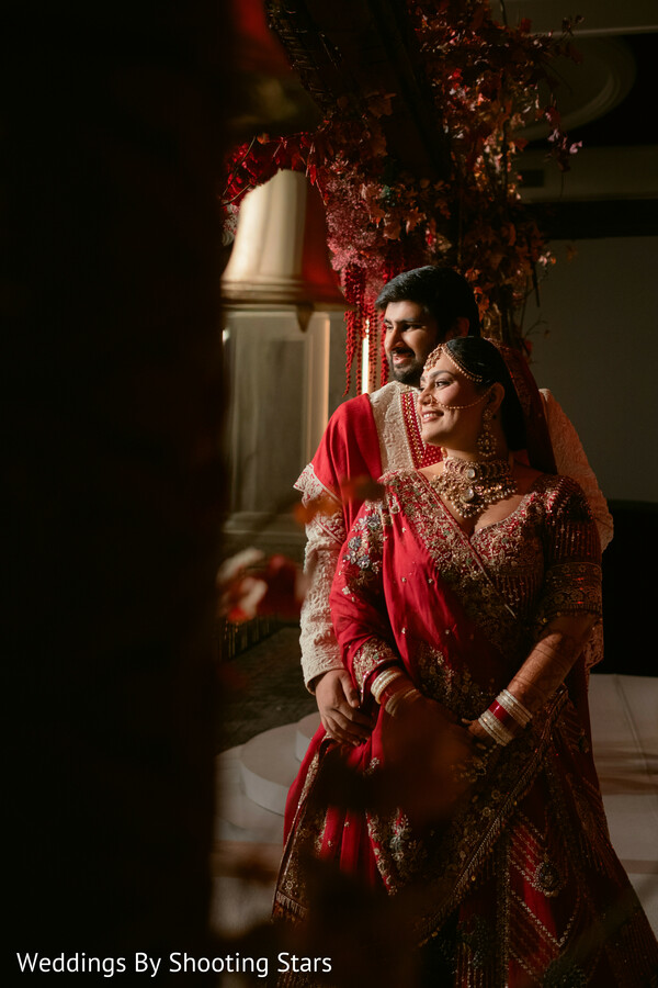 romantic couple portrait,red bridal lehenga,groom ivory sherwani,warm lighting decor,intimate wedding moment,luxury decor backdrop,indian wedding couple,emotional connection,elegant styling,moody portrait