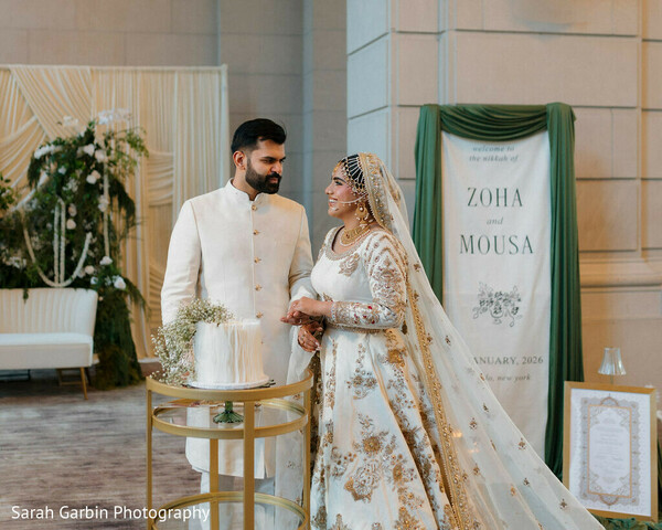 wedding cake display,couple portrait modern,ivory wedding outfits,welcome sign decor,minimalist wedding design,bride white lehenga,groom ivory sherwani,reception styling,elegant indoor wedding,soft neutral palette