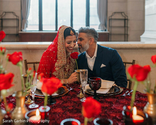 romantic dinner setup,red floral tablescape,candlelight wedding decor,couple intimate moment,bride red lehenga,groom navy suit,reception styling,luxury table decor,moody wedding vibe,elegant dining