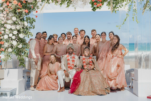 wedding party group photo,beach wedding ceremony,floral arch decor,bridesmaids peach outfits,groomsmen coordinated attire,destination wedding group,oceanfront ceremony,couple seated portrait,wedding guests celebration,tropical wedding vibes