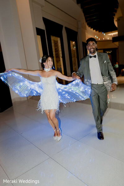 bride groom running,reception entrance moment,led wings bride,couple candid fun,wedding party energy,modern wedding vibes,playful couple moment,reception celebration,bride short dress,groom tuxedo style