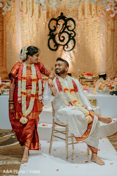 south indian wedding ceremony,bride red saree,groom white dhoti,floral garlands couple,ceremony candid moment,playful couple pose,indian wedding rituals,temple style decor,joyful wedding moment,cultural celebration