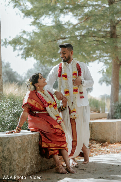 south indian wedding attire,bride red silk saree,groom white dhoti,couple garlands,outdoor wedding portrait,traditional indian couple,candid romantic moment,temple jewelry bride,natural light wedding,cultural wedding portrait