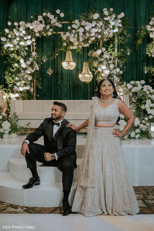 reception stage portrait,bride ivory lehenga,groom black tuxedo,floral backdrop decor,luxury wedding stage,confident bride pose,modern indian wedding,elegant couple styling,wedding photography pose,indoor reception decor