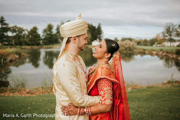 indian wedding couple portrait,lakeside wedding photo,bride red saree,groom cream sherwani,romantic couple gaze,outdoor wedding setting,bridal jewelry detail,cultural wedding attire,natural light portrait,intimate wedding moment