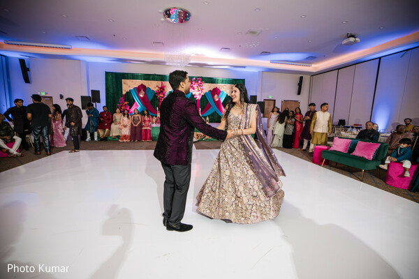 couple dance performance,sangeet celebration,bride purple lehenga,groom formal jacket,joyful couple moment,wedding entertainment,dance floor spotlight,indian wedding event,candid celebration,lively crowd