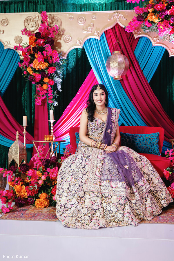 bridal portrait stage,colorful wedding backdrop,floral decor setup,bride lehenga portrait,sangeet stage styling,vibrant draping decor,indian bride jewelry,solo bridal pose,event design details,wedding decor inspiration