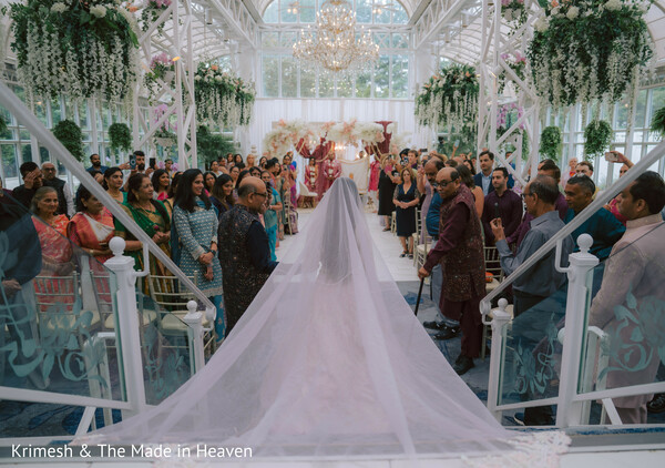 bride veil long train,ceremony aisle view,indoor garden wedding,glasshouse ceremony,floral decor overhead,bride walking aisle,wedding ceremony moment,elegant venue design,romantic wedding scene,bridal entrance dramatic