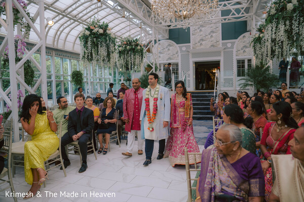 groom ceremony entrance,indoor wedding aisle,glasshouse venue decor,floral hanging installation,indian wedding ceremony,guests seated ceremony,groom baraat indoors,elegant venue setting,wedding rituals moment,cultural ceremony