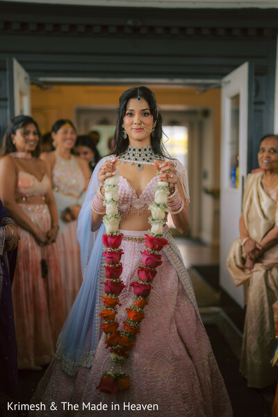 bride holding varmala,pink lehenga bridal look,wedding ceremony moment,bridal entrance indoor,indian wedding traditions,garland exchange ritual,bridal jewelry details,emotional wedding moment,bride walking candid,cultural ceremony