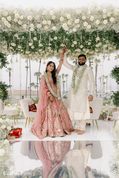 ceremony couple portrait,floral mandap white decor,indian wedding ceremony,bride pink lehenga,groom ivory sherwani,newlywed celebration,romantic wedding moment,elegant ceremony setup,luxury wedding decor,joyful couple