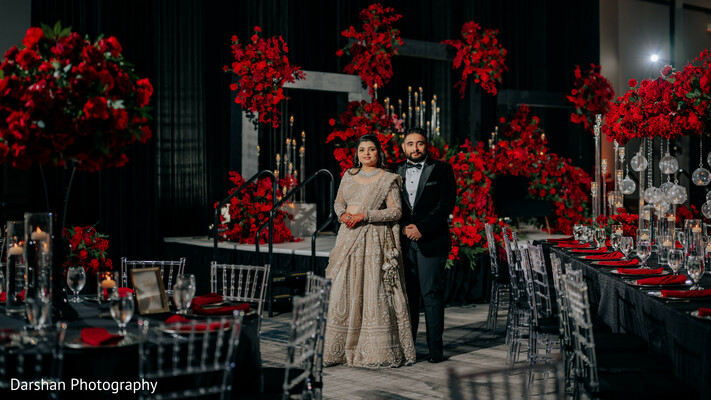 indian wedding reception,luxury wedding decor,red floral decor,couple portrait reception,elegant couple,black tie wedding,wedding stage design,dramatic wedding setup,candlelight decor,reception styling