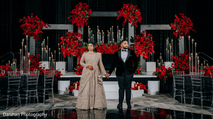 couple walking,wedding reception entrance,bride and groom,luxury wedding decor,romantic couple,red floral decor,candlelight wedding,elegant reception,indian wedding,newlyweds