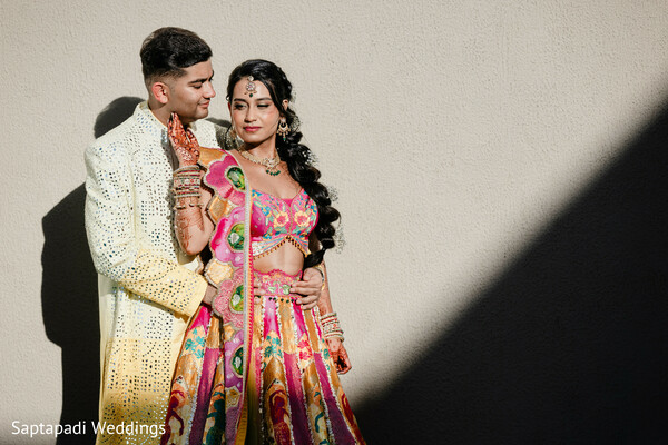 couple portrait,colorful lehenga,embroidered sherwani,floral backdrop,romantic embrace,pre wedding celebration,mehndi outfit,destination wedding,wedding fashion,bride and groom