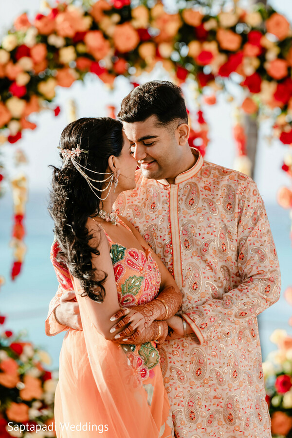 oceanfront wedding,floral mandap,peach lehenga,embroidered sherwani,romantic embrace,destination wedding,bride and groom portraits,luxury wedding decor,seaside romance,wedding fashion