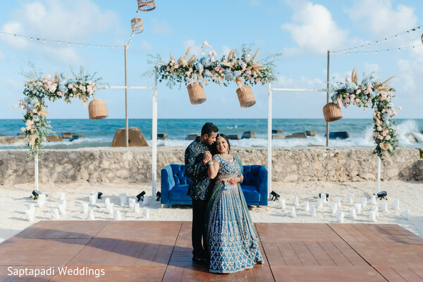 oceanfront wedding,couple portraits,blue lehenga,floral backdrop,destination wedding,beach reception,romantic embrace,coastal celebration,wedding fashion,bride and groom
