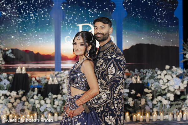 navy blue lehenga,embroidered sherwani,floral decor,candle decor,starry backdrop,couple portrait,elegant attire,blue and white flowers,romantic setting,wedding fashion