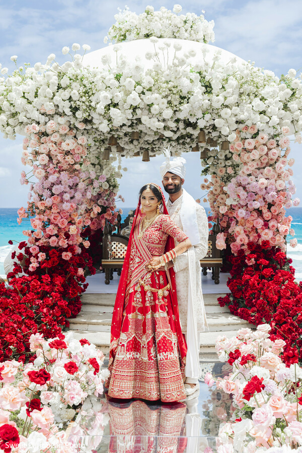 floral arch,floral decor,red lehenga,white sherwani,bridal fashion,groom fashion,ocean backdrop,rose decor,south asian wedding