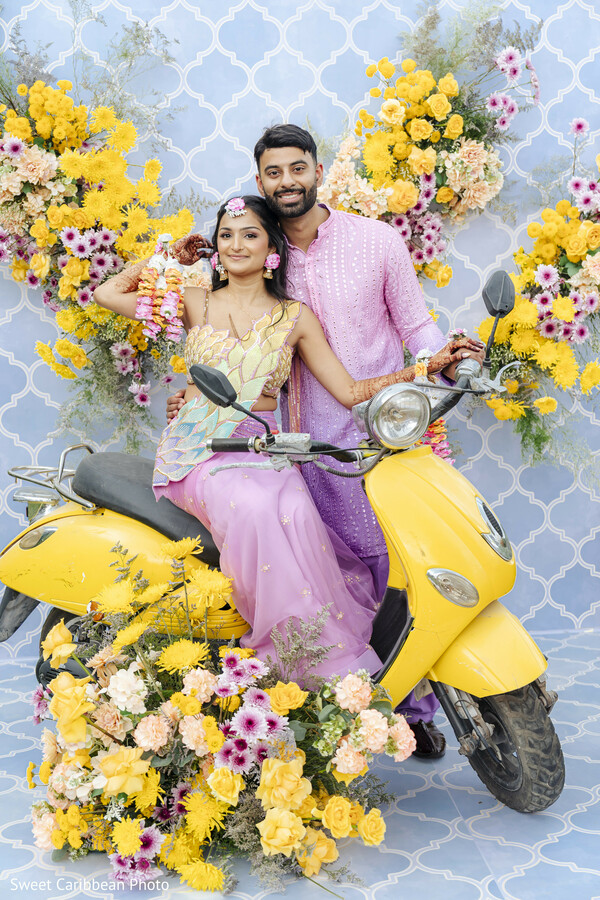 couple portrait,yellow scooter,floral decor,pink kurta,colorful lehenga,blue backdrop,vibrant colors