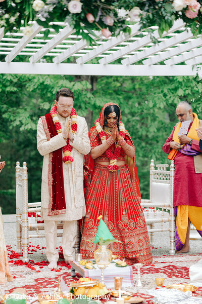 south asian wedding,outdoor ceremony,red lehenga,white sherwani,floral decor,mandap,rose petals,hindu wedding,traditional attire,wedding ceremony