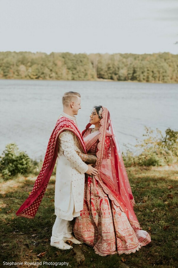 outdoor portraits,red lehenga,white sherwani,red dupatta,bridal fashion,groom fashion,lake backdrop,couple photography,wedding attire,embroidered lehenga