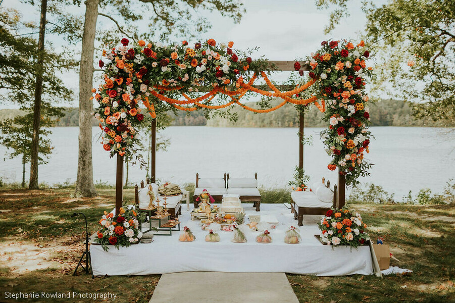 mandap,floral decor,outdoor ceremony,wedding altar,orange flowers,red flowers,lake view,wedding decor,ceremony stage,floral arch