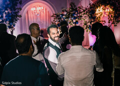 Groom's Joyful Interaction Amidst Vibrant Reception Lighting