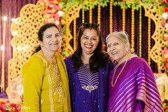 Three Women in Traditional Attire Smiling Against Floral Archway