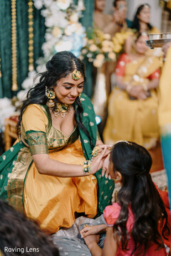 Woman in Yellow and Green Outfit with Floral Jewelry Adorns Child's Forehead