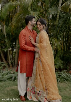 Couple in Gold Lehenga and Orange Kurta Amidst Lush Greenery
