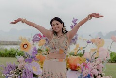 Bride in Embroidered Lehenga with Arms Outstretched Amidst Colorful Floral Decor