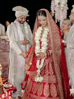 Bride in Red Lehenga and Groom in Light Sherwani with Floral Malas