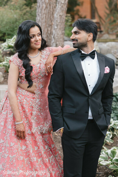blush pink lehenga,embroidered lehenga,groom suit,black suit,bridal jewelry,wedding fashion,couple photo,outdoor portrait,pink pocket square