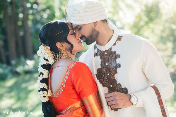 couple portrait,red top,white sherwani,floral accents,bridal hair,groom attire,outdoor setting,traditional attire