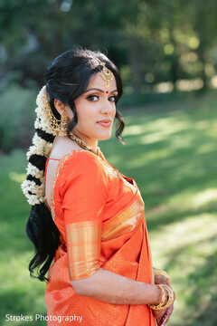 Bride in Orange Sari with Floral Braided Hairstyle and Gold Jewelry