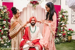 Groom's Turban Being Adjusted by Two Women Amidst Floral Decor