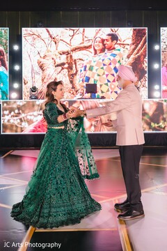 Bride in Emerald Green Lehenga Poses with Man Before LED Screen Display