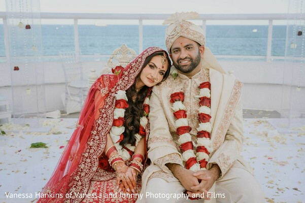 couple portrait,wedding garlands,water backdrop,red outfit,cream suit,outdoor wedding,floral garlands