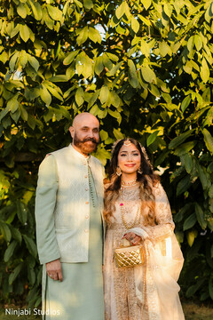 Father and Daughter in Traditional Attire Against Green Foliage