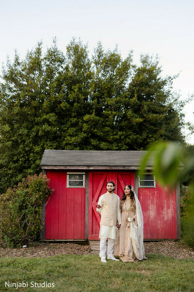 couple portrait,outdoor wedding,rustic backdrop,red shed,cream sherwani,cream bridal fashion,wedding photography,natural setting