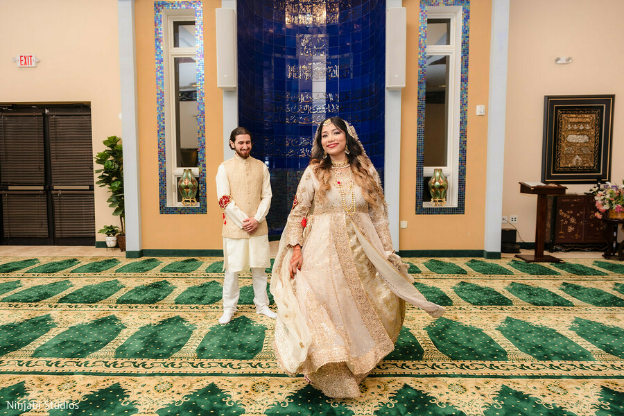 south asian wedding,off-white anarkali,gold kurta pajama,nehru jacket,elegant attire,patterned carpet,blue wall decor,couple portrait,traditional fashion,wedding fashion,wedding inspiration
