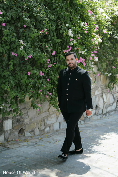 Groom in Black Sherwani Poses by Floral Wall