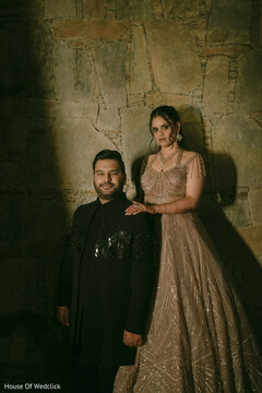 Couple in Champagne Lehenga and Black Sherwani Against Stone Wall