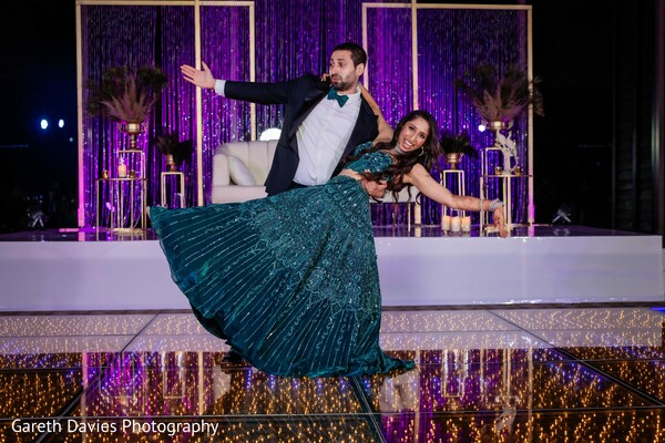 reception,teal lehenga,groom suit,couple dance,reflective floor,purple decor,gold accents,south asian wedding,wedding fashion,dance performance,stage decor,elegant reception