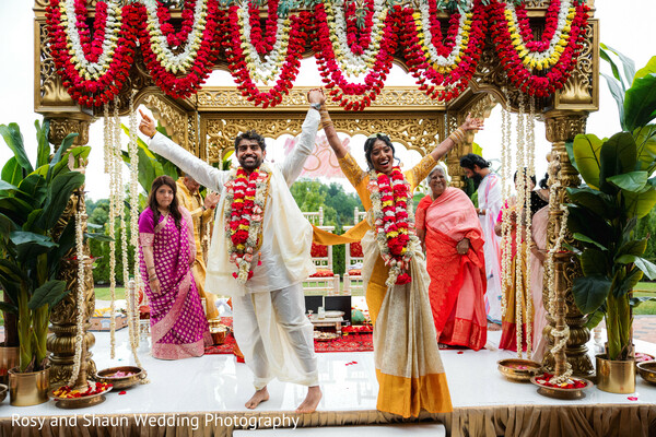 outdoor ceremony,floral mandap,red and white flowers,cream and yellow sari,cream kurta,dhoti,wedding ceremony,happy couple,mandap decor