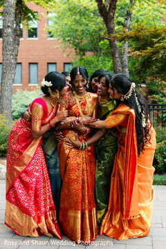 Bride in Orange and Gold Sari Embraced by Women in Colorful Saris