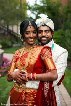 Smiling Couple in Red and Ivory Wedding Attire Embracing Outdoors