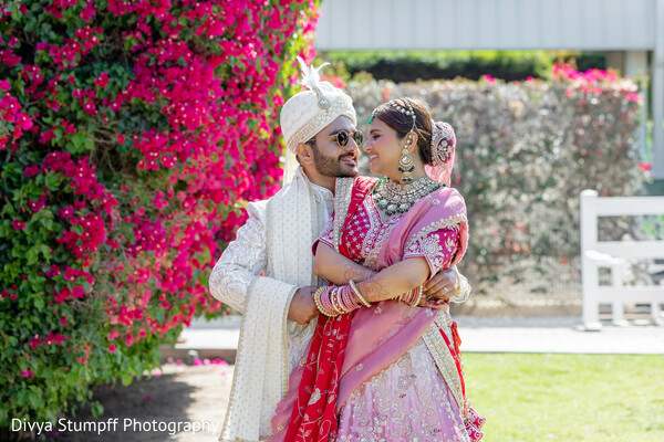 south asian wedding,couple portrait,pink lehenga,red dupatta,cream sherwani,bridal jewelry,groom fashion,outdoor wedding,vibrant florals,bougainvillea